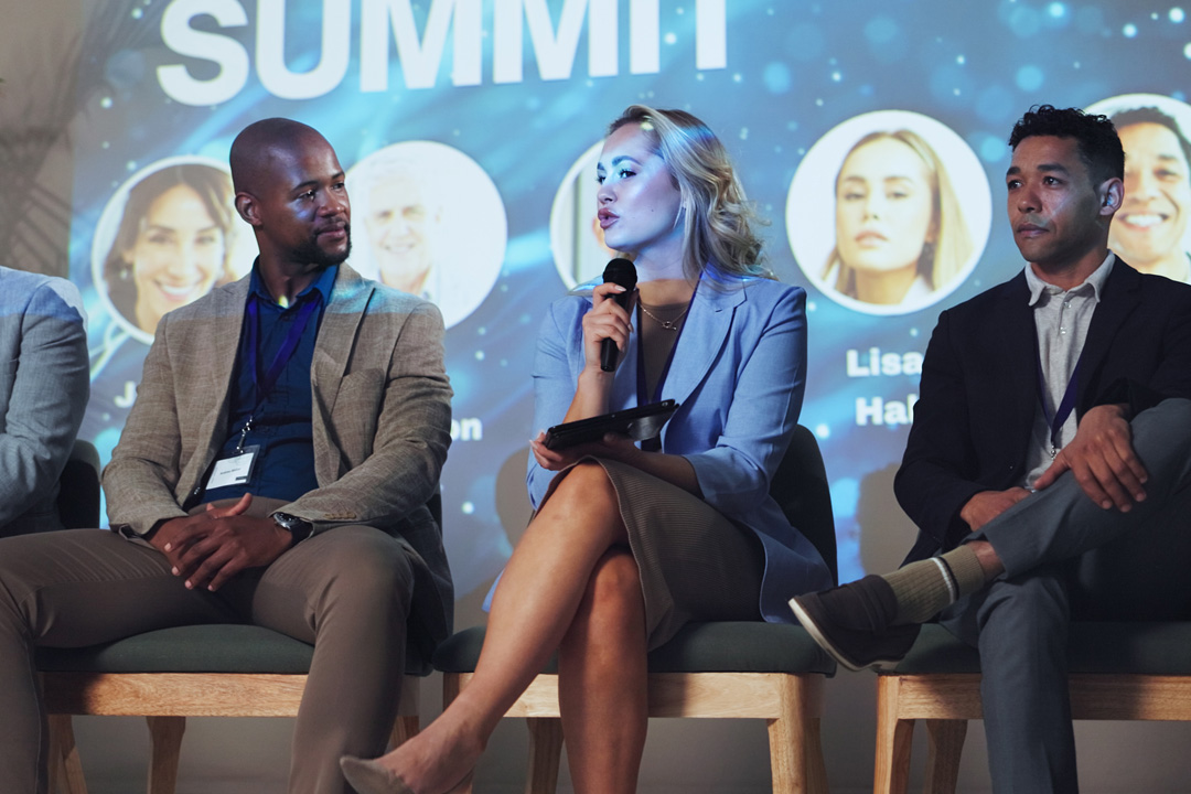 Panelists seated on stage at a business summit in front of a presentation screen